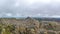 A scenic view of a rocky mountain summit with a stony cairn and mountain range in the background under a stormy grey cloudy sky