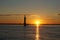 Scenic view of a silhouette of a lighthouse in a tranquil lake reflecting the sunset