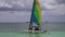 Scenic view at small catamaran with yellow green blue sail sailing in sea.