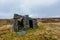 A scenic view of a stony mountain shelter in ruin surrounded with grass and bog under a grey sky