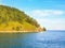 Scenic view of summer calm lake Baikal on the edge of the forest and green hill, against the blue sky