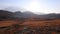 Scenic view to sun kissed field surrounded by high hills and mountains under blue sky