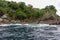 Scenic view of tropical rocky beach with trees foliage and cliff. Sea water wave and splash. For environment and geology.