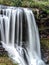 A scenic waterfall roadside going over the cliff down to the boulders and rocks below where you can no longer drive under but can