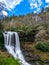 A scenic waterfall roadside going over the cliff down to the boulders and rocks below where you can no longer drive under but can