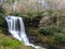 A scenic waterfall roadside going over the cliff down to the boulders and rocks below where you can no longer drive under but can