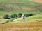 A scenic west yorkshire pennine country landscape with sheep grazing in stone walled hillside fields with an old farmhouse