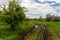 Scenic wet after rain dirt muddy road through trees and green grass field meadows against blue sly background. Russian rural