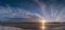 Scenic wide panorama of spring sunset over melting icy lake. Beautiful red yellow orange Sun, dark blue and white clouds on blue