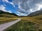 Scenic, winding road leading to a stunning valley, with cloudy skies and lush green grass