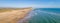 A scenics aerial panoramic view of a sandy beach with hill cliff in the background along a beautiful choppy blue see under a