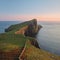 A scennery of a fine lighthouse standing on a stunning cliff against the backdrop of the sea and lit by the setting sun