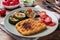 Schnitzel of chicken and zucchini cooked on the grill. Fresh tomatoes on a plate. Ready delicious dinner lunch. Wooden background