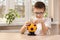 School-age boy with glasses sitting at the table. He holds a 100 zloty banknote in his hands which he puts into a football-shaped