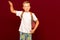 School boy greets as captain with backpack, on red wall