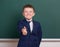 School boy show best gesture, portrait near green blank chalkboard background, dressed in classic black suit, one pupil, education