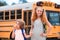 School bus and Happy Children. Portrait of happy little brother and sister standing together in front of school bus.