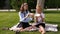 School children sitting in the park on the grass and holding large sandwiches.