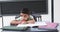 In a school classroom, a young biracial boy sits at a desk