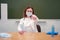 School doctor with medical masks in hand by the blackboard and pointing at you, copy space