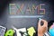 School exams concept with exam word from colourful pencils on blackboard background with school supplies
