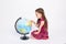 A school girl sits on a white isolated background with a globe and searches for countries with her finger, September 1, knowledge