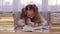 School girl at table thinking about homework and writing in a school notebook