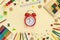 School and office supplies border with red alarm clock  on beige paper background. Multicolored pencils, paints, plasticine,