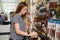 School stationery and art shop. Female customer chooses paintbrushes. Seller arranges painting supplies on display shelf