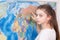 A school student girl studies geography on a large map of the world on the wall