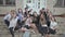 School students sit on the steps of the school and wave their hands. Group Of High School Students Sitting Outside