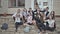 School students sit on the steps of the school and wave their hands. Group of high school students sitting outside