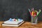 School supplies such as textbook, notebook, pens, pencils, scissors over chalkboard background