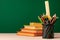 School supplies on wooden desk against green chalkboard