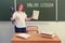 A school teacher holds a camera on a tripod standing at the blackboard with the text