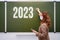 A school teacher in a medical mask with the text 2023 in the classroom