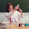 A school teacher sits in a chemistry class and conducts experiments with reagents in test tubes. A woman at the teacher desk looks