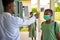 School teacher wearing a lab coat, taking temperature reading of school pupil