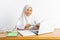 school veiled girl at desk reading book while using laptop