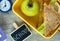 School yellow lunch box with sandwich, green apple, pencils, clock on black chalkboard. Healthy eating at school.