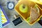 School yellow lunch box with sandwich, green apple, pencils, clock on black chalkboard. Healthy eating at school.