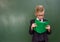 Schoolboy with book near empty green chalkboard