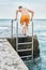 Schoolboy climbs up pier on ladder against clear seascape