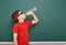 Schoolboy drink water from bottle near a blackboard, empty space, education concept