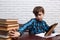 Schoolboy with electronic book pushing back a stack of books. No