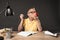 schoolboy in eyeglass eating apple and doing homework at table with lamp books colour pencils and textbook on grey