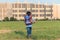 The schoolboy happily runs with a backpack on the field against the background of the city landscape