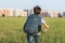 The schoolboy happily runs with a backpack on the field against the background of the city landscape