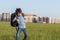 The schoolboy happily runs with a backpack on the field against the background of the city landscape