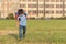 The schoolboy happily runs with a backpack on the field against the background of the city landscape